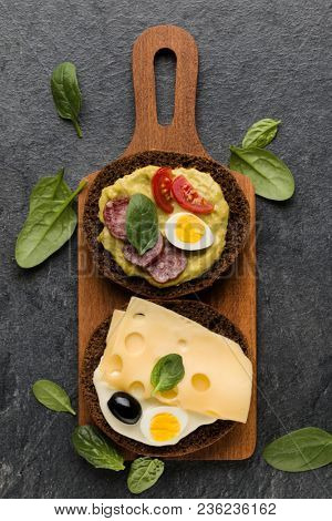 Open faced sausage sandwich canape or crostini on a wooden serving board  on dark stone background closeup. Top view.