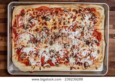 Over Head Photograph Of A Homemade Red Pizza That Has Been Cooked With Sliced Tomato, Bacon, And Mus