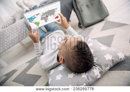 Interactive Map. Young Afro American Boy Using Tablet While Lying On His Back