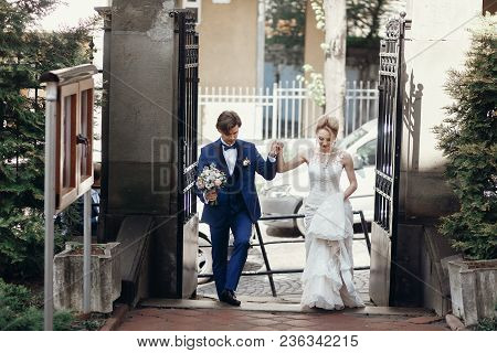 Stylish Groom And Bride Walking And Holding Hands In City Street, Hugging And Embracing. Wedding Day