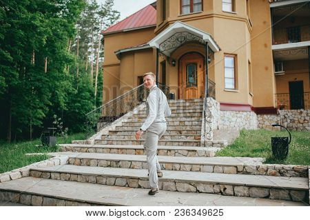 Groom In The Stylish Wedding Suit Going To The Bride With A Bouquet Of Flowers. Back View