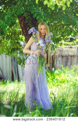 Attractive Young Girl With Blonde Dren Hair And Natural Make-up Smelling Blue Purple Iris Flowers On