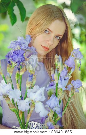 Attractive Young Girl With Blonde Dren Hair And Natural Make-up Smelling Blue Purple Iris Flowers On