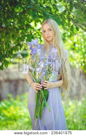 Attractive Young Girl With Blonde Dren Hair And Natural Make-up Smelling Blue Purple Iris Flowers On
