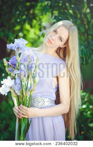 Attractive Young Girl With Blonde Dren Hair And Natural Make-up Smelling Blue Purple Iris Flowers On