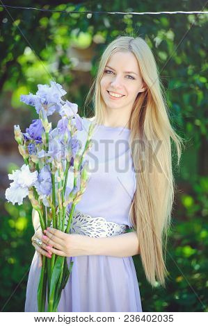 Attractive Young Girl With Blonde Dren Hair And Natural Make-up Smelling Blue Purple Iris Flowers On