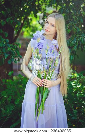 Attractive Young Girl With Blonde Dren Hair And Natural Make-up Smelling Blue Purple Iris Flowers On
