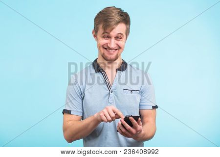 Funny Man Texting Message On Smart Phone Isolated On Grey Background. Smiling Guy Holding Smartphone