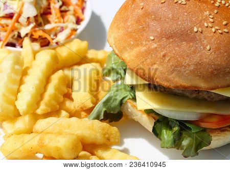 Hamburger With Beef, Cheese And Vegetables On White Plate With French Fries And Salad Onside. Closeu