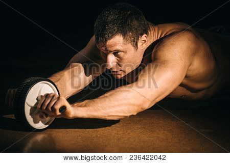A Fitness Man Shakes A Press With A Wheel. Isolated Dark Background