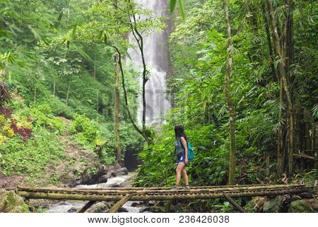 Tourist woman crossing a bamboo bridge near the Red Coral waterfall in the Munduk jungle, Bali, Indonesia