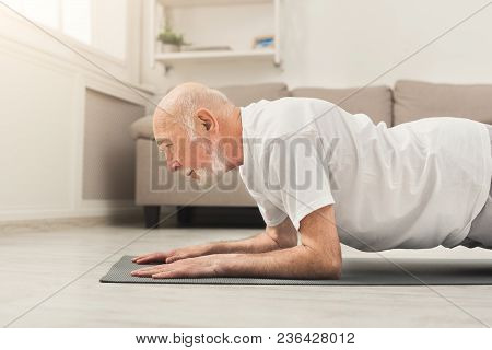 Senior Man Workout At Home. Side View On Mature Caucasian Guy Making Plank Or Push Ups Exercise. Act