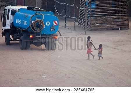 JUBA, SOUTH SUDAN-DECEMBER 1, 2010: An unidentified woman walks with her children in Juba, South Sudan as a water truck goes by.