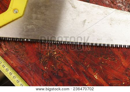 Work In Carpentry Shop. Saw And Measuring Tape Lie On Dirty Workbench In Carpentry Workshop. Tools F
