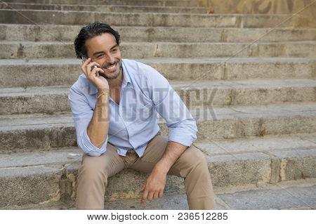 Young Attractive Latin Man On City Staircase Talking Happy On Mobile Phone Looking Satisfied And Con