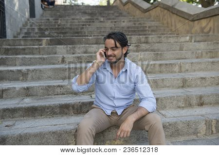 Young Attractive Latin Man On City Staircase Talking Happy On Mobile Phone Looking Satisfied And Con