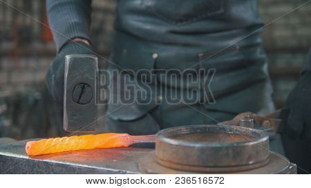 The Blacksmith With A Beard Gives Shape With The Help Of A Hammer On The Anvil To A Red-hot Metal Pr
