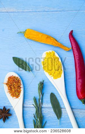 Cooking Hot Spicy Food Concept. Dry Spices And Herbs In Wooden Spoons And Chili Peppers On Blue Wood