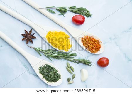 Cooking Hot Spicy Food Concept. Dry Spices And Herbs In Wooden Spoons, Fresh Herbs And Beans, White 