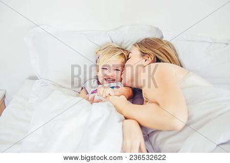Happy And Loving Mother Having Fun And Kissing Her Daughter On The Bed. Family Morning Concept. Spen