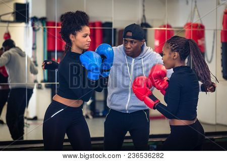 Experienced boxing trainer supervising and teaching two female boxers indoors