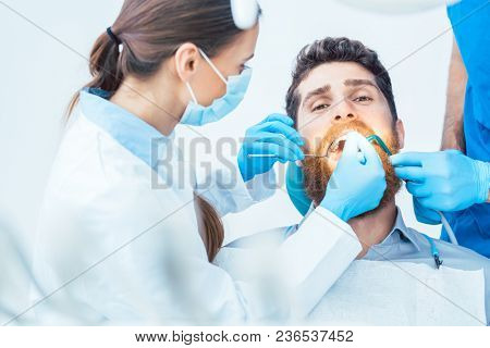 Portrait of a young man looking at camera with a relaxed facial expression, during a painless oral procedure in the modern dental office of an experienced dentist