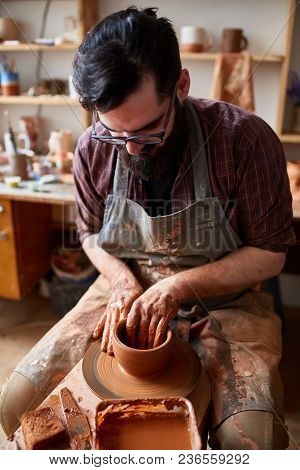 Portrait Of A Handsome Bearded Male Potter In Plaid Shirt And Dirty Apron Who Molds Bowl From Clay, 