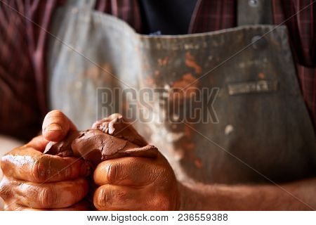 Shallow Depth Of Field Close-up Hands Of A Male Potter In Plaid Shirt And Dirty Apron Battering Clay