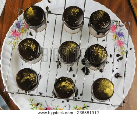 Chocolate Dessert From Mousse, Covered With Chocolate Glaze And Sprinkled With Golden Powder On A Sh