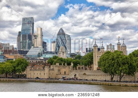 The City of London financial district, The Tower of London, Traitors Gate and the river Thames. Unidentifiable people walk along the river bank in summer