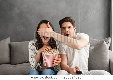 Image of caucasian uptight family sitting on sofa at home with popcorn in hand while watching scary movie