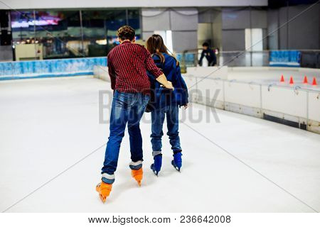 Teenage couple holding hands and ice skating together