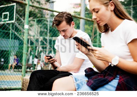 Expressionless young couple in the park using smartphones with no social interactions addiction concept