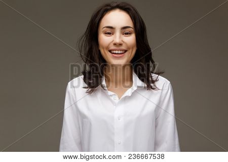 Beautiful Girl In A White Shirt Shows Emotions - Smile, Fun. On A Light Background.