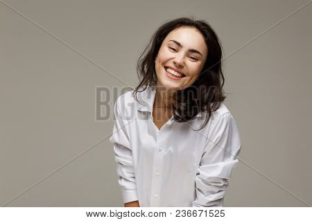 Beautiful Girl In A White Shirt Shows Emotions - Smile, Fun. On A Light Background.