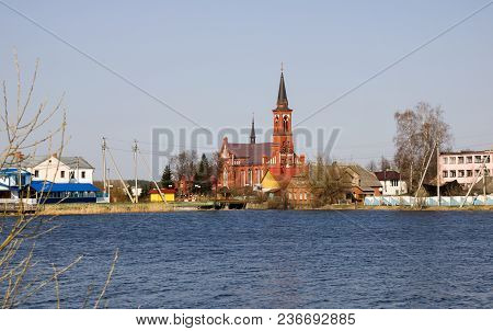 Catholic Church Of Red Brick On The River Bank, Spring