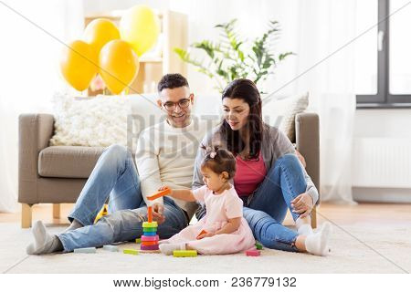 family, holidays and people concept - happy mother, father and little daughter playing with ring pyramid baby toy on birthday party at home