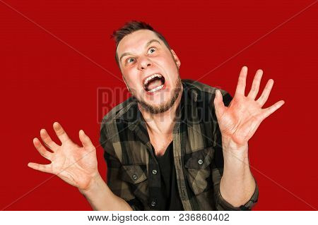 Young Smiling Guy With Beard And Modern Hairstyle, With Opened Mouth And Hands Up, Isolated On Red B