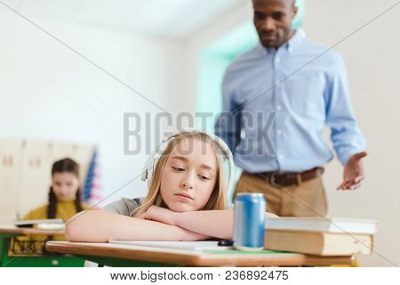 Dreamy High School Teenage Student Listening Music In Headphones With Classmate And Teacher Behind