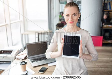 Smart And Confident Woman Is Looking To The Camera And Holding A Tablet In It. The Screen Of The Tab