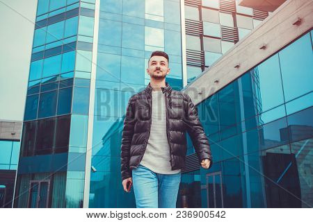 Confident Arabian Man Walking In City Center In Front Of Modern Building. Young Man Holds Smartphone