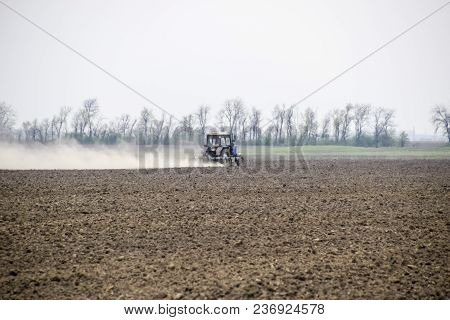 The Tractor Harrows The Soil On The Field And Creates A Cloud Of Dust Behind It.