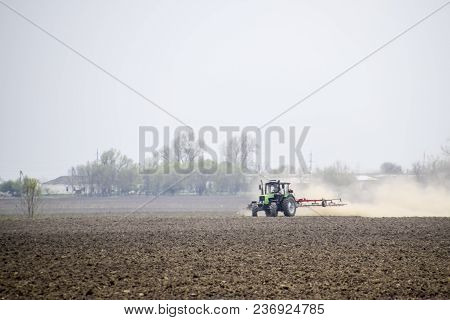 The Tractor Harrows The Soil On The Field And Creates A Cloud Of Dust Behind It.