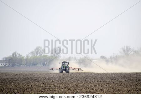 The Tractor Harrows The Soil On The Field And Creates A Cloud Of Dust Behind It.