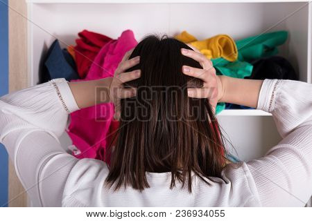 Rear View Of A Young Woman With Hand On Head In Front Of Cloth Shelf