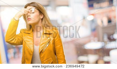 Beautiful young woman with sleepy expression, being overworked and tired, rubbes nose because of weariness at restaurant
