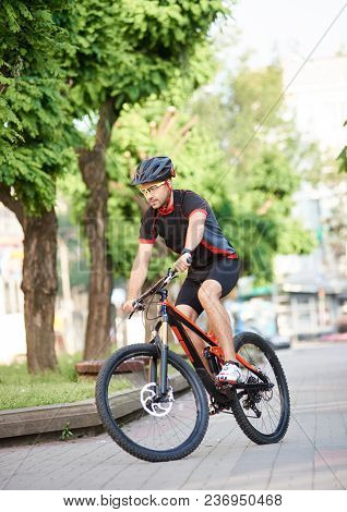 Young Male Cycler In Cycling Sportswear And Protective Gear Performing Tricks On City Streets, Getti