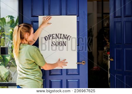 Woman putting on store opening soon sign