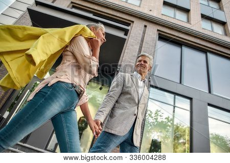 We Choose Happiness. Lovely Middle-aged Couple Holding Hands And Smiling While Walking Together Thro