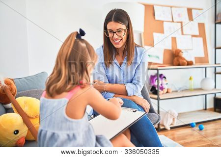 Young therapist woman speaking and treating child, counselor and behaviour correction at pedagogue payroom taking notes on clipboard